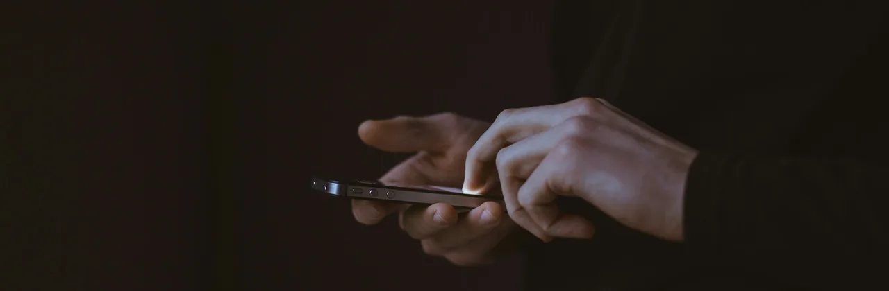Manos usando un teléfono casi a oscuras, con el borde de la pantalla iluminado